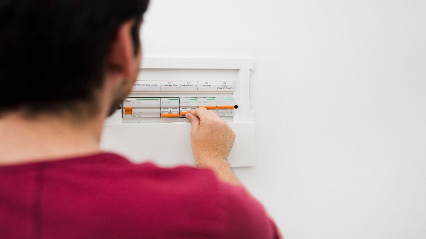 A man turning off a circuit breaker before Clean Baseboard Heaters.
