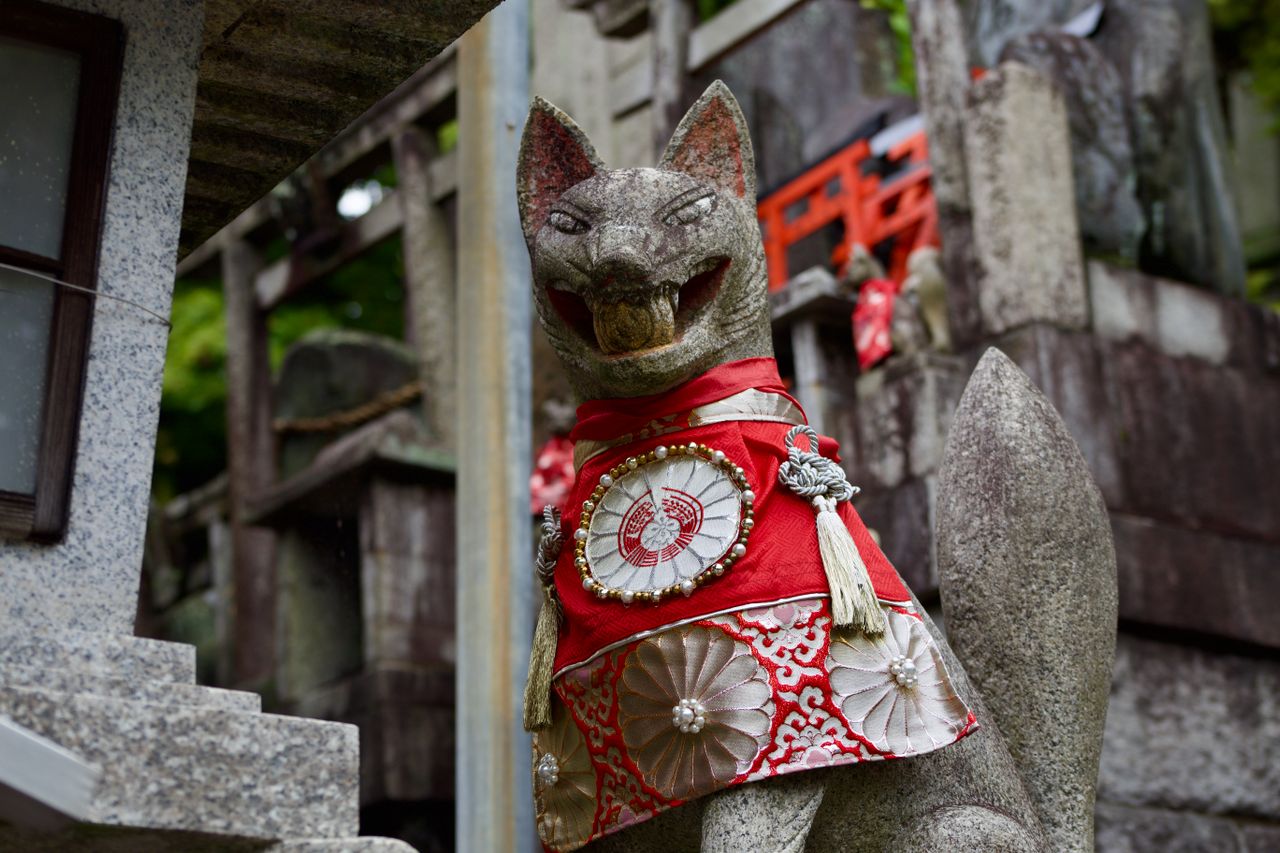 Japanese fox (kitsune) shrine statue wearing traditional red ceremonial attire