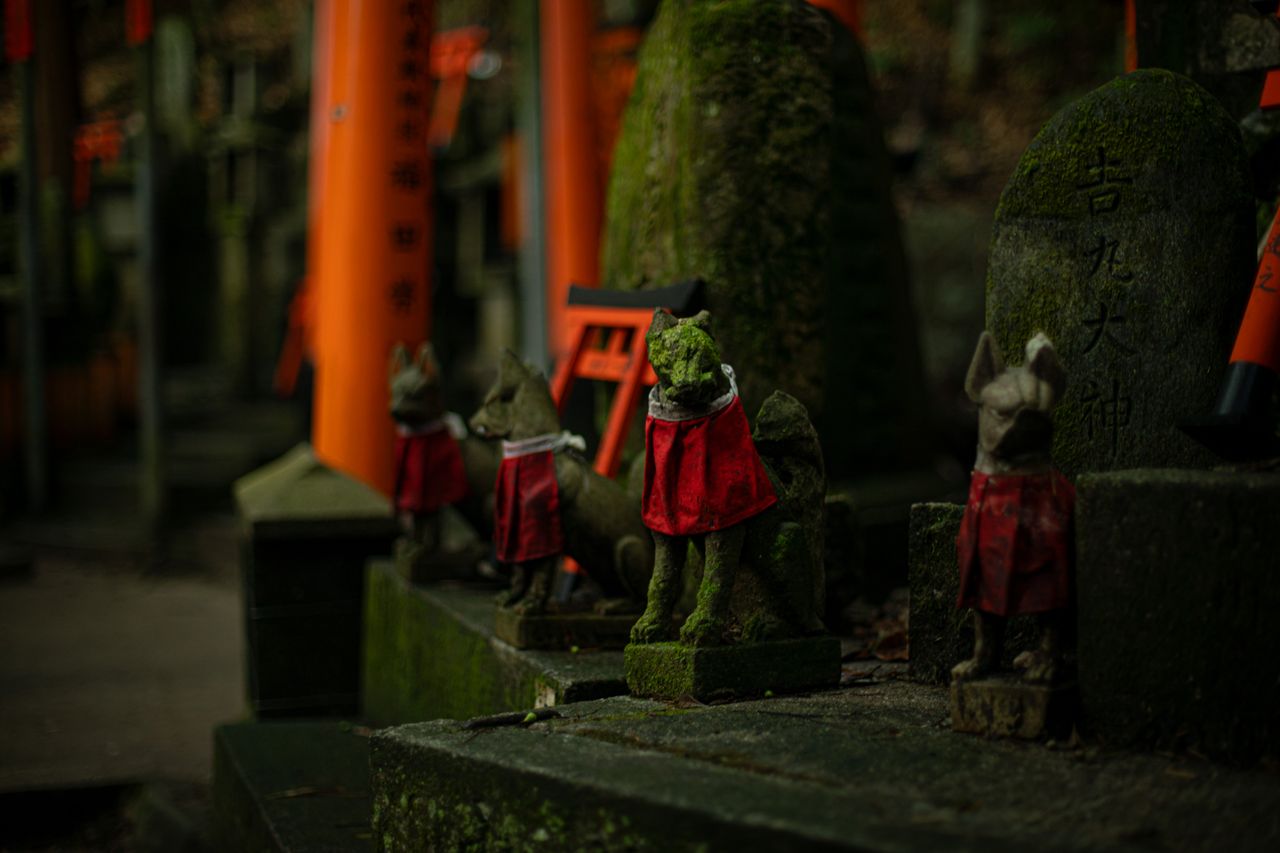 A moss-covered stone fox statue guarding a traditional Japanese shrine