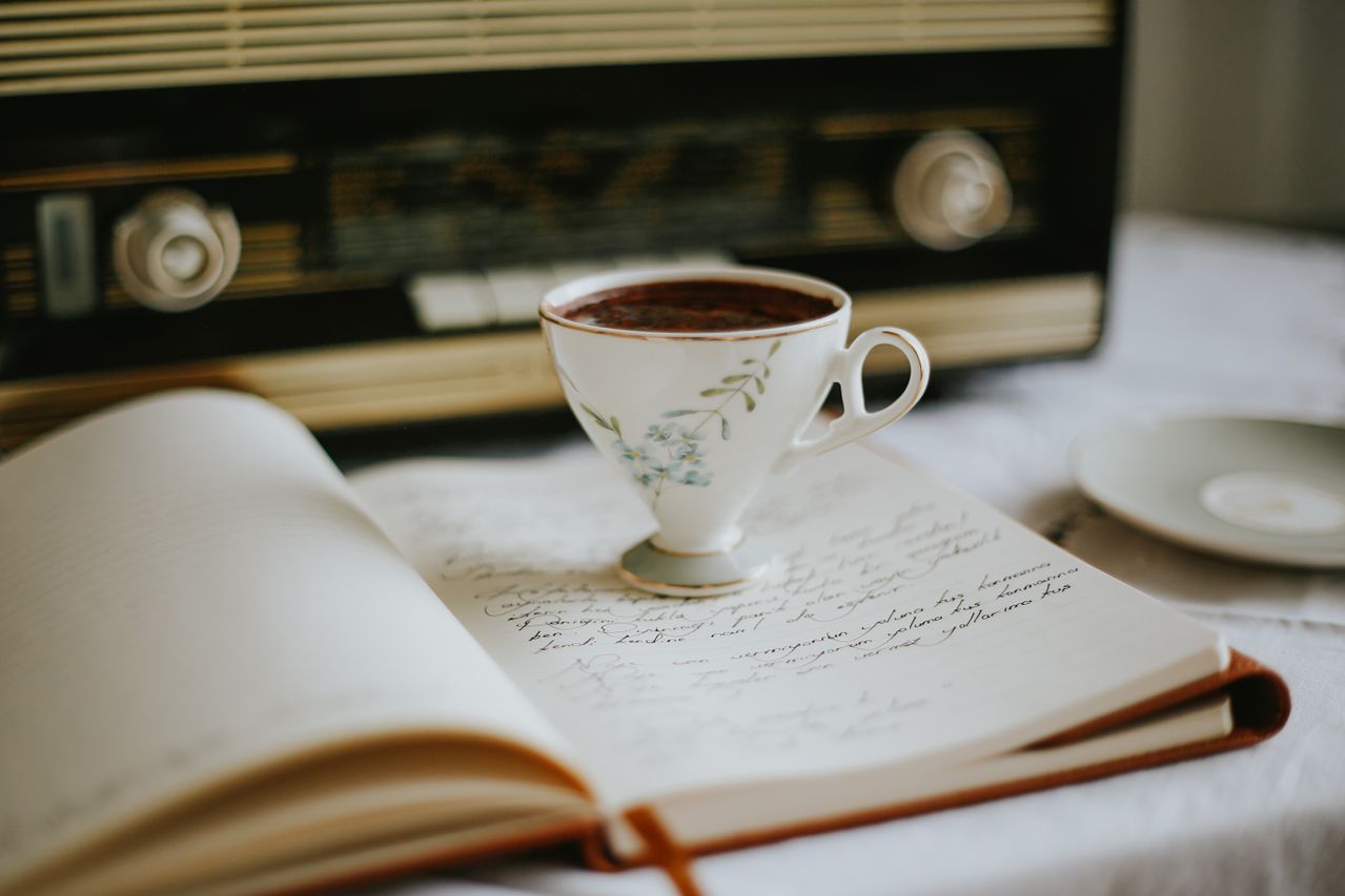 An open journal and warm cup of tea resting on a wooden table