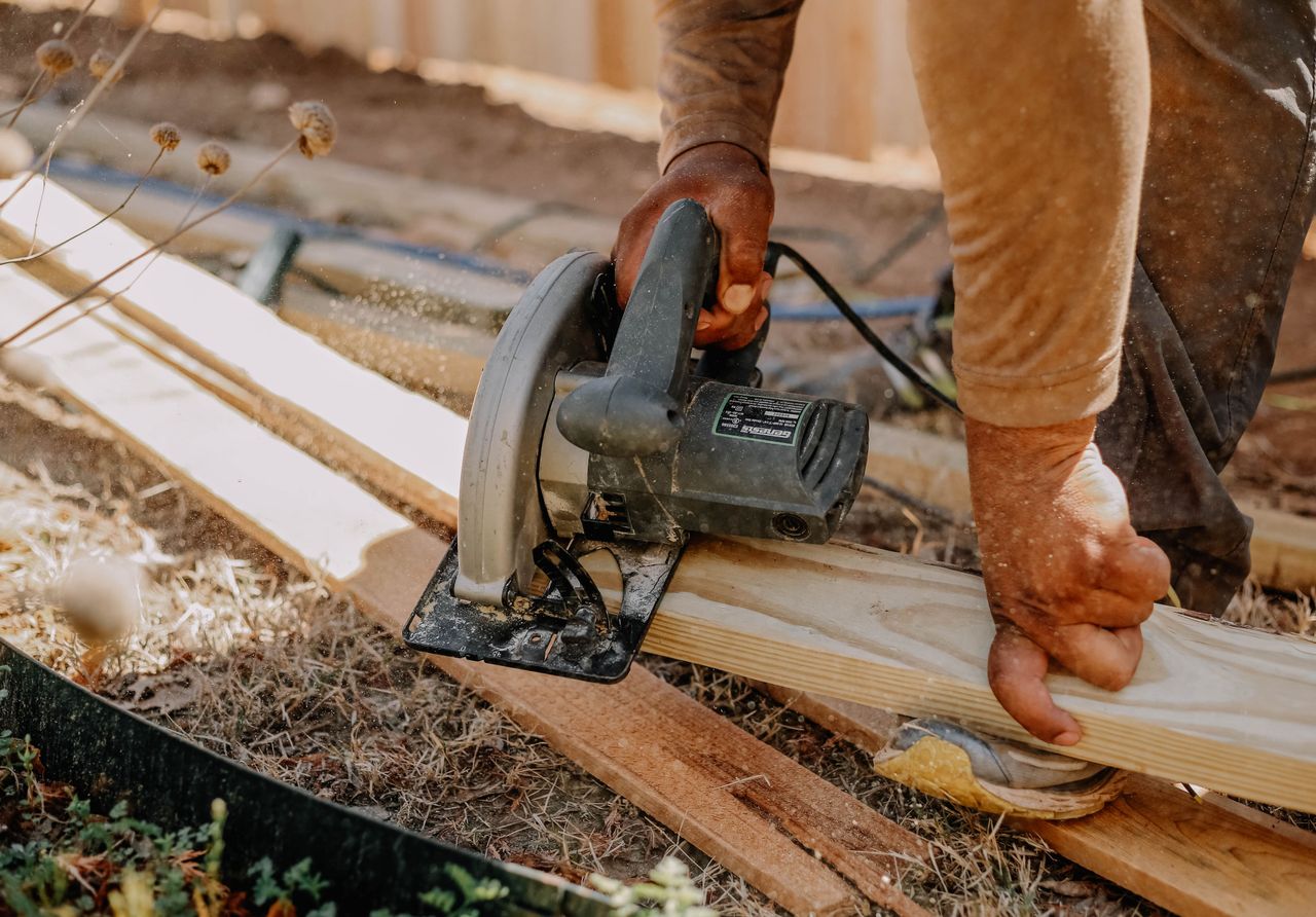 Builder attaching wire mesh to a wooden A-frame chicken coop outdoors.