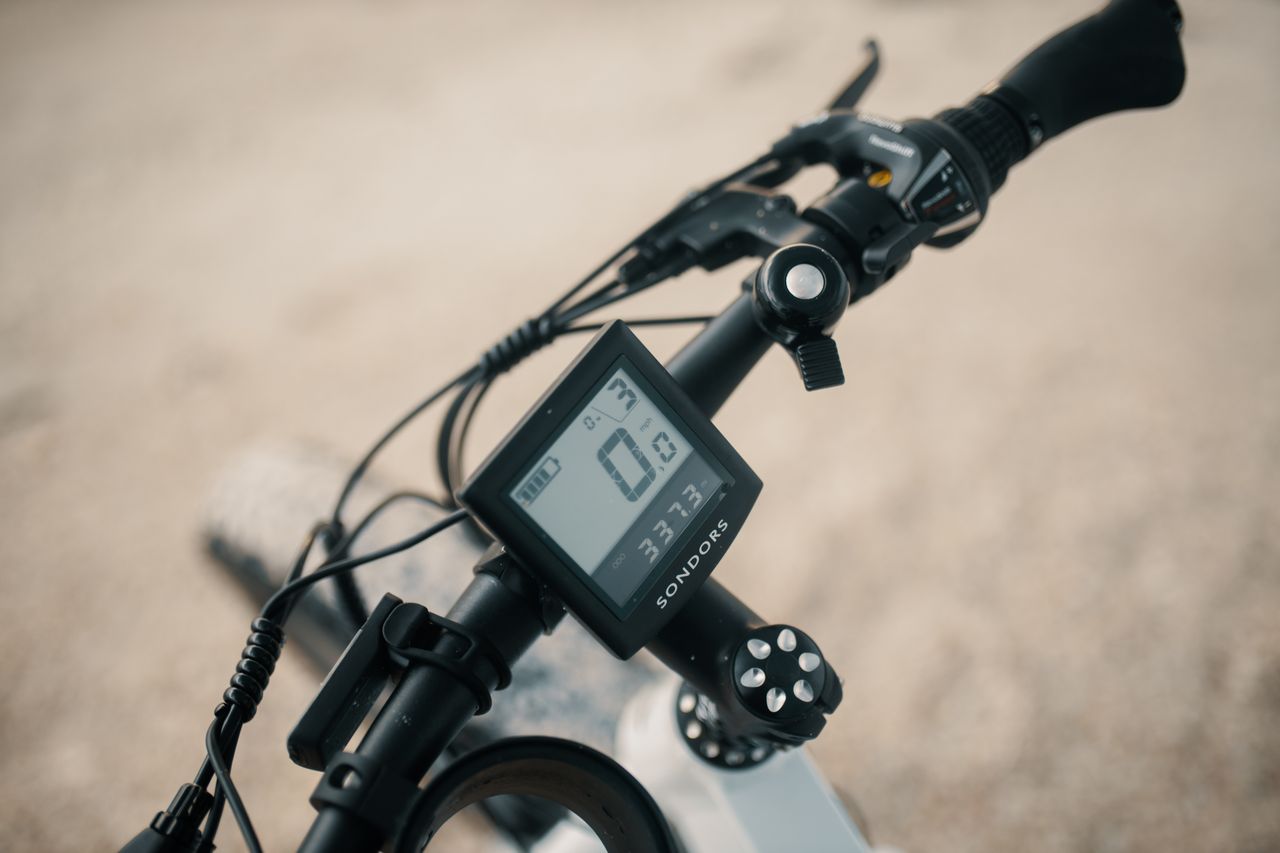 Electric bike handlebar cockpit displaying LCD screen battery indicator and gear shifters