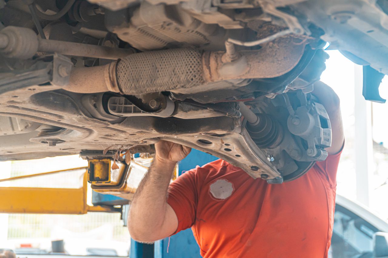 Mechanic using tools to adjust front truck suspension in a driveway garage