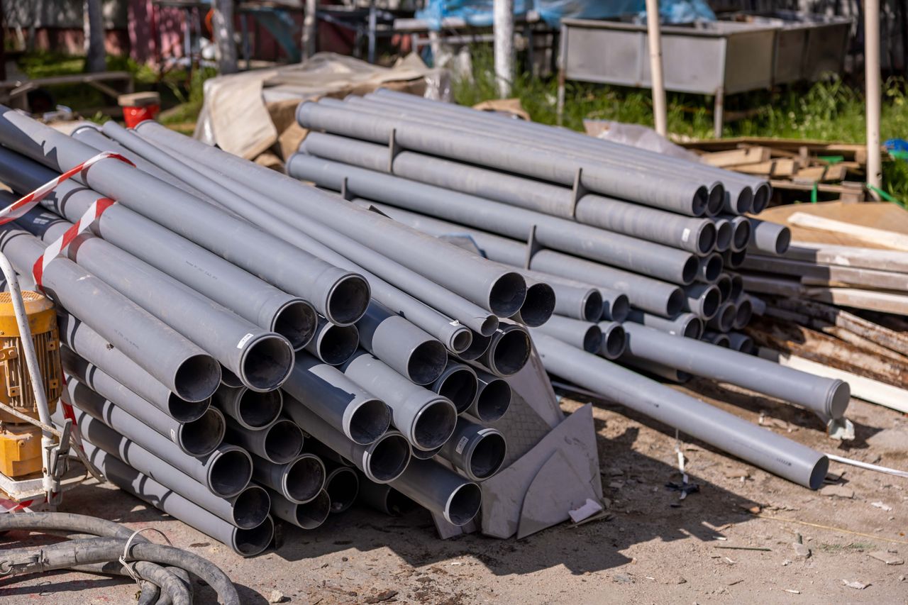 Stacked gray PVC pipes and plumbing materials at an outdoor construction site ready for septic system installation.