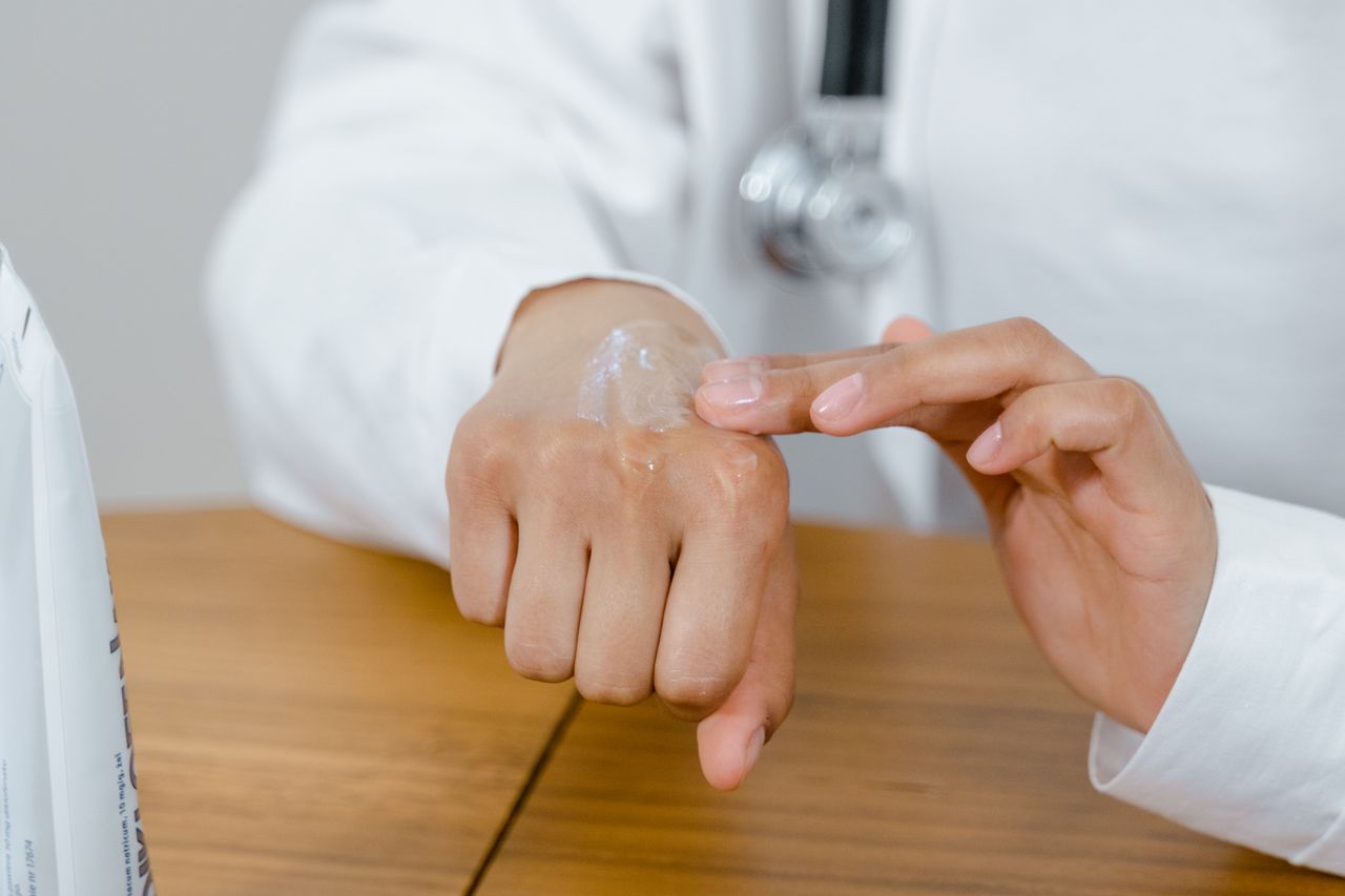 Dermatologist applying a medical silicone gel patch to a patient's healing skin during a c-section scar treatment consultation.