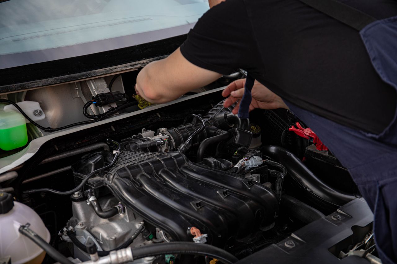 Auto technician inspecting engine hoses under the hood during a smog check.