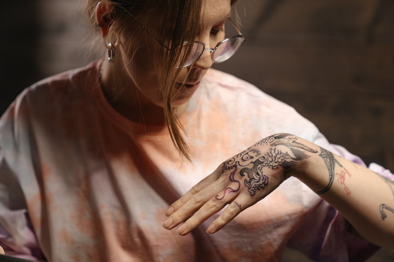A woman looks closely down at the detailed black-ink tattoo on the back of her hand.
