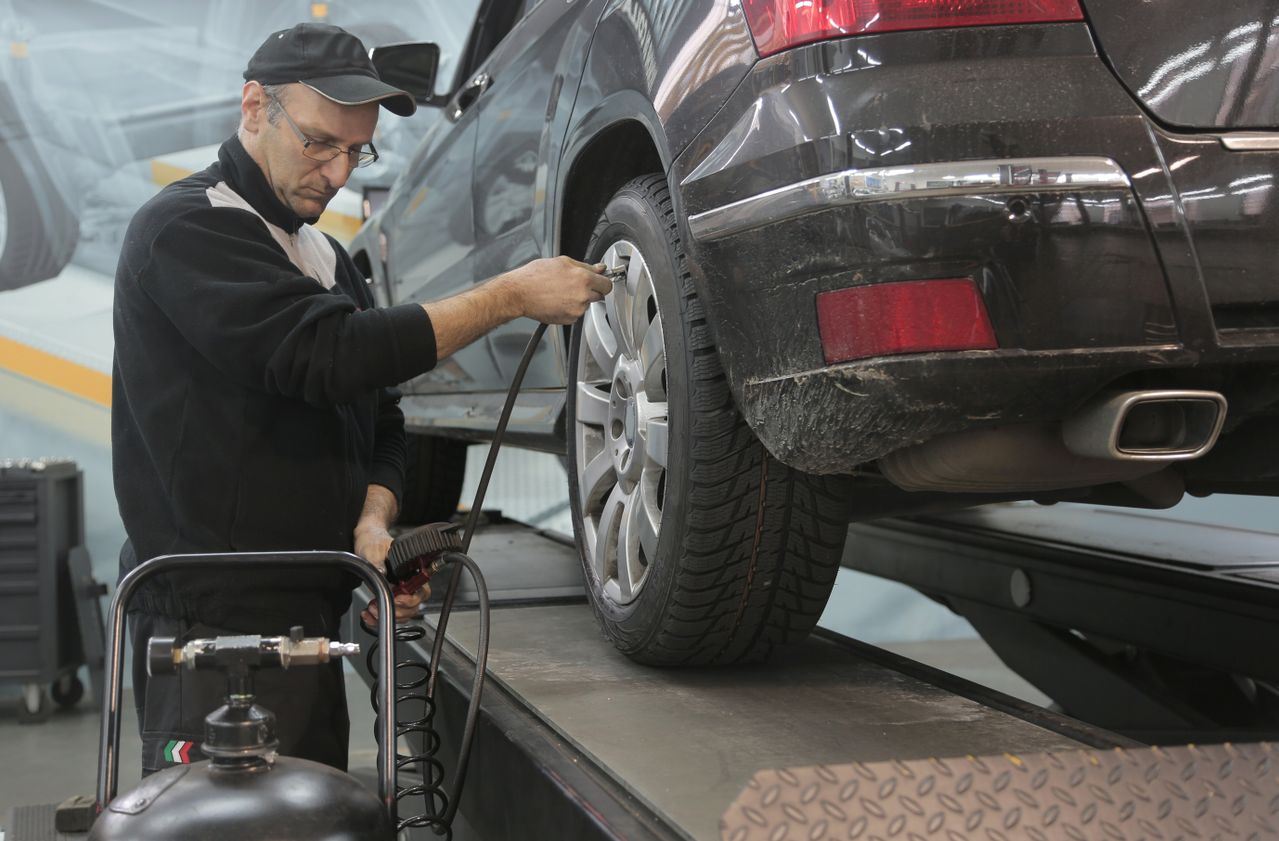 Mechanic inspecting a car tire and measuring tire pressure with a gauge in a clean automotive workshop.