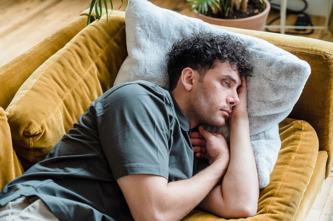Man lying on a yellow couch resting his sore shoulder at home